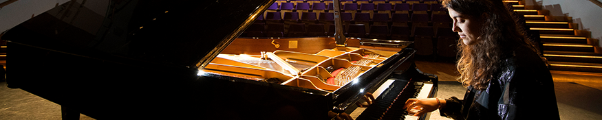Female student playing a grand piano in an empty theatre